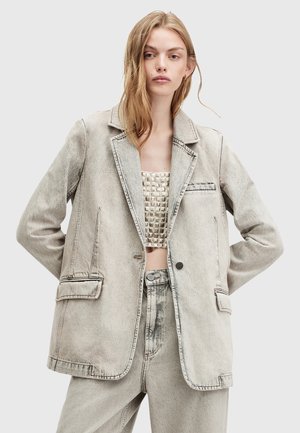 Ljust grå denimblazer med slagkrage, två framfickor och kontrasterande sömmar. Matchas med en texturerad kort topp och matchande byxor.