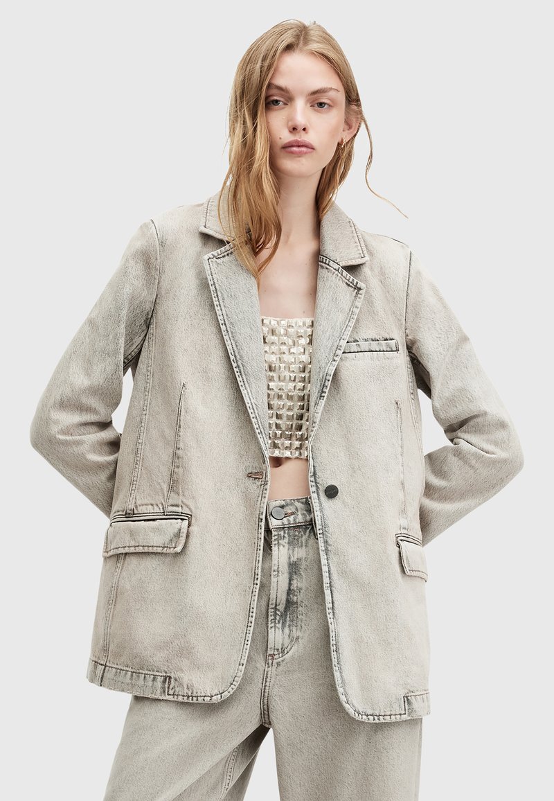 Blazer in denim grigio chiaro con rever a punta, due tasche frontali e cuciture a contrasto. Abbinato a un top cropped testurizzato e pantaloni coordinati.