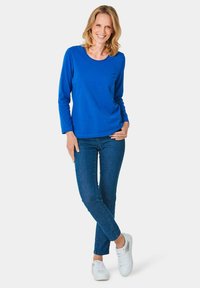 Blauwe lange mouwen shirt gecombineerd met donkere denim jeans en witte sneakers, met een ronde halslijn en zachte katoenmateriaal.