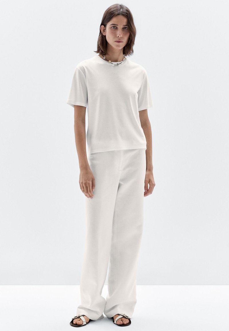 T-shirt bianco a maniche corte e pantaloni ampia abbinati in tessuto morbido. Una collana a catena notevole e sandali casual completano il look.