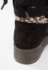Botte d'hiver en daim noir avec semelle grise texturée, revers en tricot crème et marron, et logo étoilé brodé sur le talon.