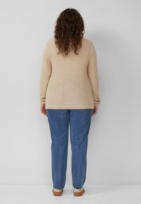 Beige gebreide trui met lange mouwen, gecombineerd met losse blauwe jeans en lichtgekleurde schoenen. Achteraanzicht, met de nadruk op de textuur van de stof en de pasvorm.