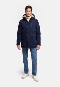 Granatowa parka z kapturem, z wyściółką z polarowego materiału, wieloma kieszeniami, regulacją sznurkiem oraz kontrastującymi tanowymi akcentami.