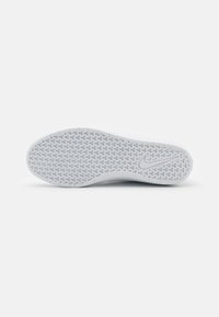 Semelle de sneaker blanche avec une surface en caoutchouc texturé. Présente un motif en chevrons et un petit logo Nike argenté sur le côté.