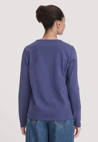Lila Langarmshirt mit Rundhalsausschnitt, aus weichem Stoff, hat eine lockere Passform und wird mit Jeanshosen kombiniert.