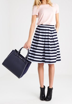 Jupe rayée bleu marine et bleu clair avec des plis, associée à un haut rose et des bottines noires. Tenant un sac à main bleu marine avec des accents contrastés.