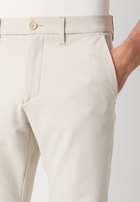 Calças bege com um corte slim, bolsos frontais, passantes para cinto e fecho de botão. Feitas de um tecido suave e leve.