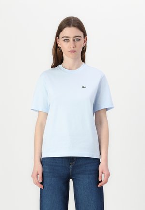 Tricou din bumbac de culoare albastru deschis, cu mâneci scurte, guler rotund și un mic logo cu crocodil verde pe pieptul stâng. Croi lejer, textură fină.