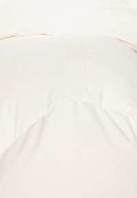 Pohovková sada v krémové barvě s hladkým, hedvábným povrchem, která má prošívaný design a elegantní, zaoblené okraje pro moderní vzhled.