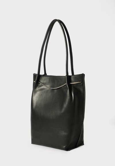 Borsa tote in pelle nera con doppi manici e un dettaglio con zip orizzontale vicino alla parte superiore su uno sfondo leggero e semplice.
