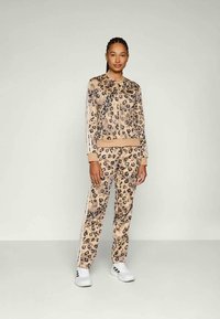 Fato de treino de padrão de leopardo feito de tecido macio, apresentando uma jaqueta com fecho e calças combinando com riscas brancas nas laterais. Ténis brancos completaram o visual.