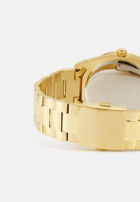 Ceas de mână din metal auriu cu finisaj lustruit, are un brățară din linkuri, cadran pătrat și închidere cu clemă. Dispune de un design minimalistic.