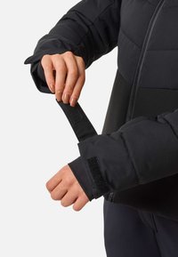 Zwarte pufferjack met een ritssluiting en klittenbandsluiting bij de manchetten. Het materiaal lijkt glad en is licht gevoerd voor isolatie.