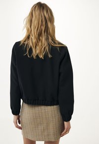 Czarna krótka kurtka z elastycznym pasem, z długimi rękawami i gładką fakturą. W połączeniu z teksturowaną żółto-szaro-kremową spódnicą.