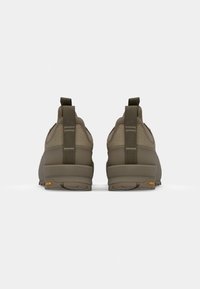 Produkt cechuje się teksturowanym, oliwkowym materiałem, zaokrąglonym kształtem i uchwytem z tyłu. Logo Vibram jest widoczne na podeszwie.