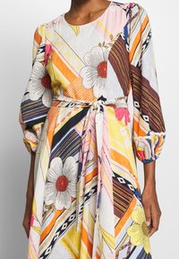 Robe multicolore avec des motifs floraux et géométriques, longue manches ballon, taille nouée et texture de tissu léger.