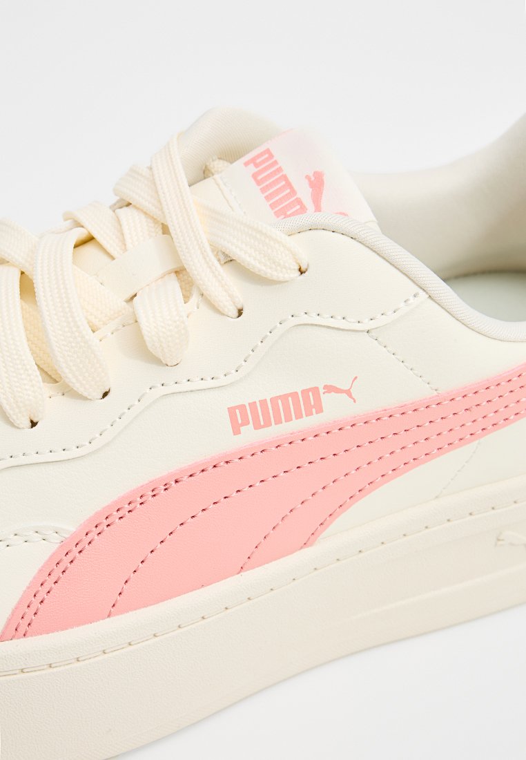 Cremefarbene Sneaker mit pinkem Puma-Logo und Akzenten, flachen Schnürsenkeln und einer strukturierten Gummisohle. Stylisches Design mit glatten Materialien.