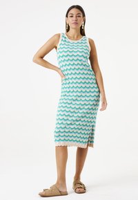 Enganliegendes Midikleid aus Strickstoff mit einem wellenförmigen Muster in Türkis, Weiß und Pink. Verfügt über einen runden Halsausschnitt und einen gewellten Saum.