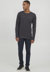 Langemouwen donkergrijs shirt met een ronde hals, gecombineerd met marineblauwe slim-fit broek en zwarte sneakers. De stof lijkt zacht en glad.
