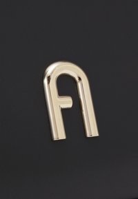 Zlatni metalski logo u obliku malog slova "a" na teksturiranoj crnoj pozadini, sa glatkom, sjajnom završnom obradom i jasnim dizajnom.