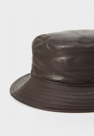 Bruine leren emmerhoed met een afgeronde top en brede, gestikte rand. Glad oppervlak met subtiele glans en ton-sur-ton stiksels.