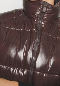 Bordeauxfarbene Pufferjacke mit hohem Kragen, glänzender Textur, Reißverschluss und horizontalen Nähten. Keine sichtbaren Logos oder Muster.