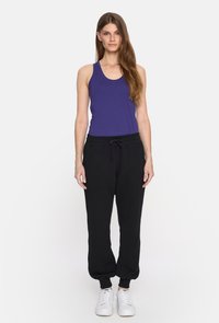 Fioletowy top na ramiączkach z tyłem w stylu racerback, w połączeniu z czarnymi dresami z elastycznym pasem i mankietami, zestawiony z białymi sneakerami.