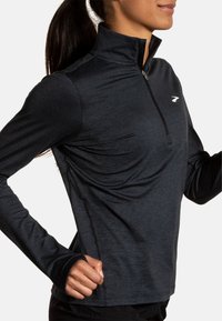 Črni dolgo rokav quarter-zip vrh iz lahkotnega, teksturiranega materiala z izrezi za palce in majhnim logotipom na prsih.