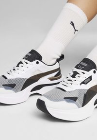 Sneaker atletiche bianche e grigie con una tomaia in mesh testurizzato, dettagli neri, suole spesse e un logo a contrasto sulla linguetta e sul lato.