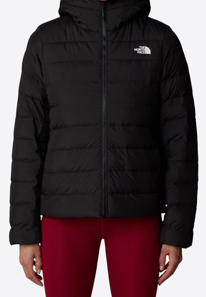 Veste noire matelassée à capuche North Face zippée, portée avec un pantalon rouge, vue de face montrant le torse et les bras.