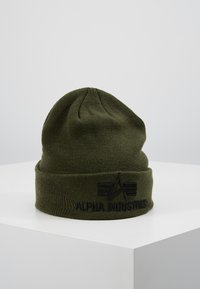 Olive green knitted beanie with a folded cuff, featuring black embroidered "ALPHA INDUSTRIES" logo and triangular design detail.