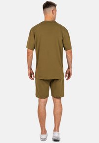 Completo di maglietta a maniche corte e pantaloni corti in verde oliva, realizzato in tessuto morbido. Presenta una vestibilità comoda con cuciture visibili e un design minimale.