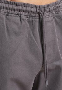 Gray drawstring pants made of cotton blend fabric, featuring an elastic waistband and textured surface with visible stitching details.