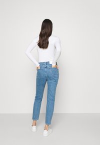 Jeans de mezclilla azul claro con una cintura alta, diseño de pierna recta, bolsillos traseros y detalles de costura sutiles, combinados con zapatillas blancas.