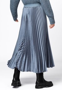 Fållad satinklänning i ljusblått med en figursydd midja, flödande design och slät textur, kombinerad med svarta chunky ankelstövlar.