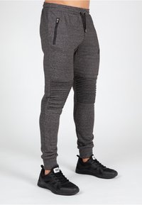 Mørkegrå tapered joggers med ribbede knædetaljer, elastisk talje og lynlåslommer, parret med sorte træningssko.