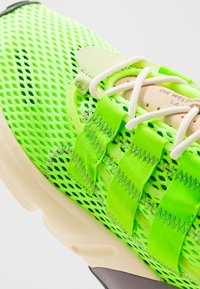 Helle grüne Mesh-Sneaker mit verstellbaren Riemen und weißen Schnürsenkeln. Merkmale eine strukturierte, gepolsterte Sohle und kontrastierende cremefarbene Akzente.
