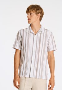 Camicetta a maniche corte con bottoni in strisce verticali bianche e beige, caratterizzata da un colletto alla francese e una leggera texture del tessuto.