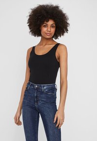 Débardeur noir à larges bretelles et encolure arrondie, associé à un jean bleu taille haute avec une texture denim classique et un léger délavage.