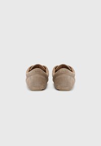Chaussures slip-on en daim beige avec une forme arrondie, présentant une texture lisse et un logo subtil au niveau du talon. Doublure intérieure douce.