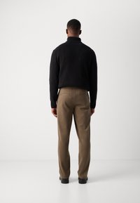 Pull à col roulé noir côtelé associé à un pantalon kaki. Le pantalon présente une coupe droite et des poches arrière, conçu pour un ajustement décontracté.