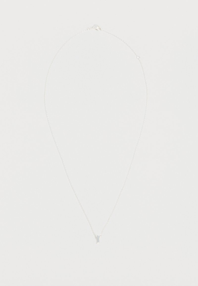 Collier délicat en chaîne argentée avec un petit pendentif en forme de lettre minuscule « r » sur un fond blanc uni.