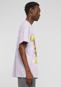 Lyselilla oversized bomulds t-shirt med et farverigt grafikprint foran, rund hals og korte ærmer.