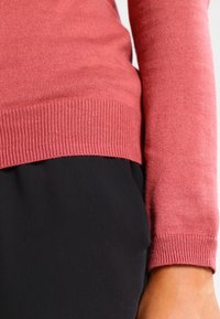 Jersey de punto color rosa coral con puños y cintura acanalados, combinado con tejido negro. Textura suave, diseño ajustado y acabado liso.