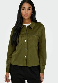 Olive green suede shirt jacket with two chest pockets and black buttons. Features a collared neckline and long sleeves with cuff detailing.