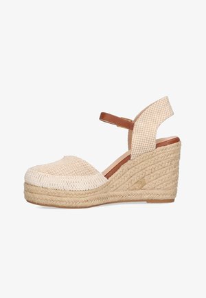 Sandales compensées beiges avec une tige tissée, bout ouvert et une bride cheville marron. Le talon est en jute tressé, apportant texture et hauteur.