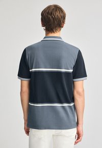 Pikétröja med mörkblå och ljusgrå färgblock, med vita ränder. Tillverkad av mjukt tyg, kort ärm och med krage.