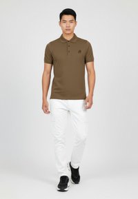 Camisa polo marrón de manga corta y cuello, combinada con pantalones cargo blancos. El conjunto presenta un diseño minimalista y sin patrones visibles.