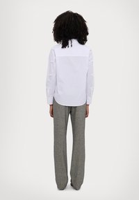 White collared shirt with long sleeves, designed with a yoke and subtle embroidery details, paired with wide-legged, textured gray trousers.