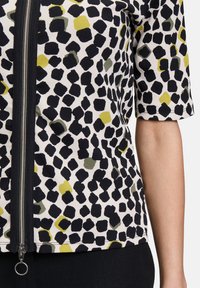 Czarny, żółty i zielony top w wzory z prążkowaną teksturą, z zamkiem błyskawicznym z przodu i krótkimi rękawami. Zbliżenie na detale materiału.